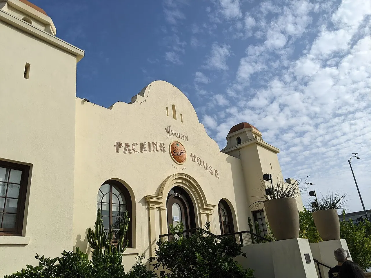 The Spanish-style facade of the Anaheim Packing House under a blue sky with scattered clouds.
