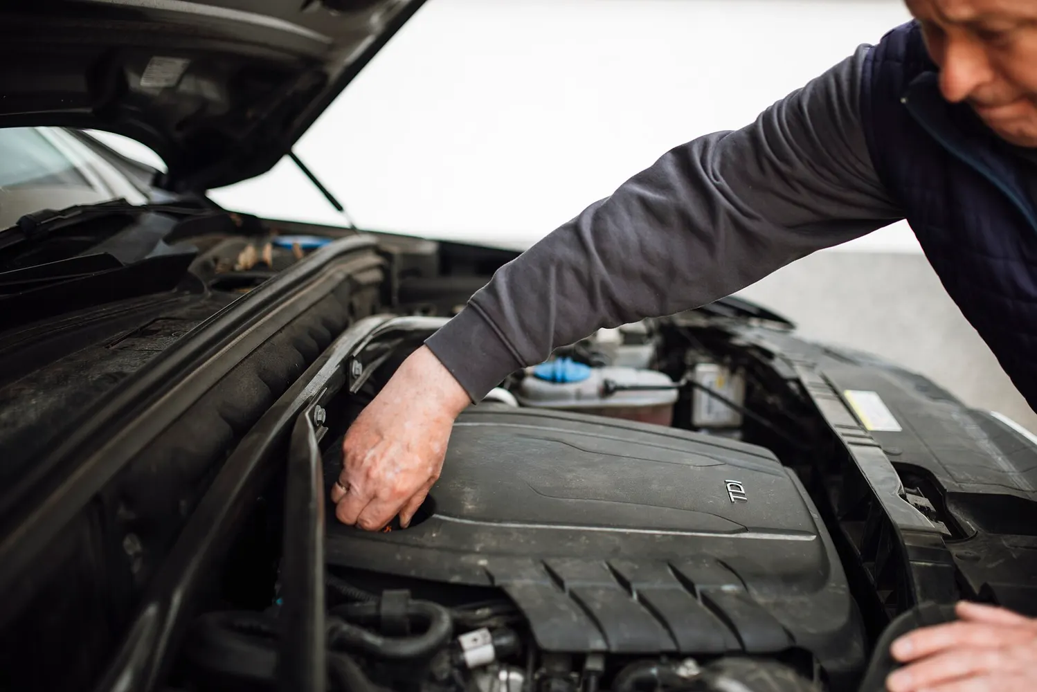 A mechanic reaches into the open engine bay of a car during routine maintenance.