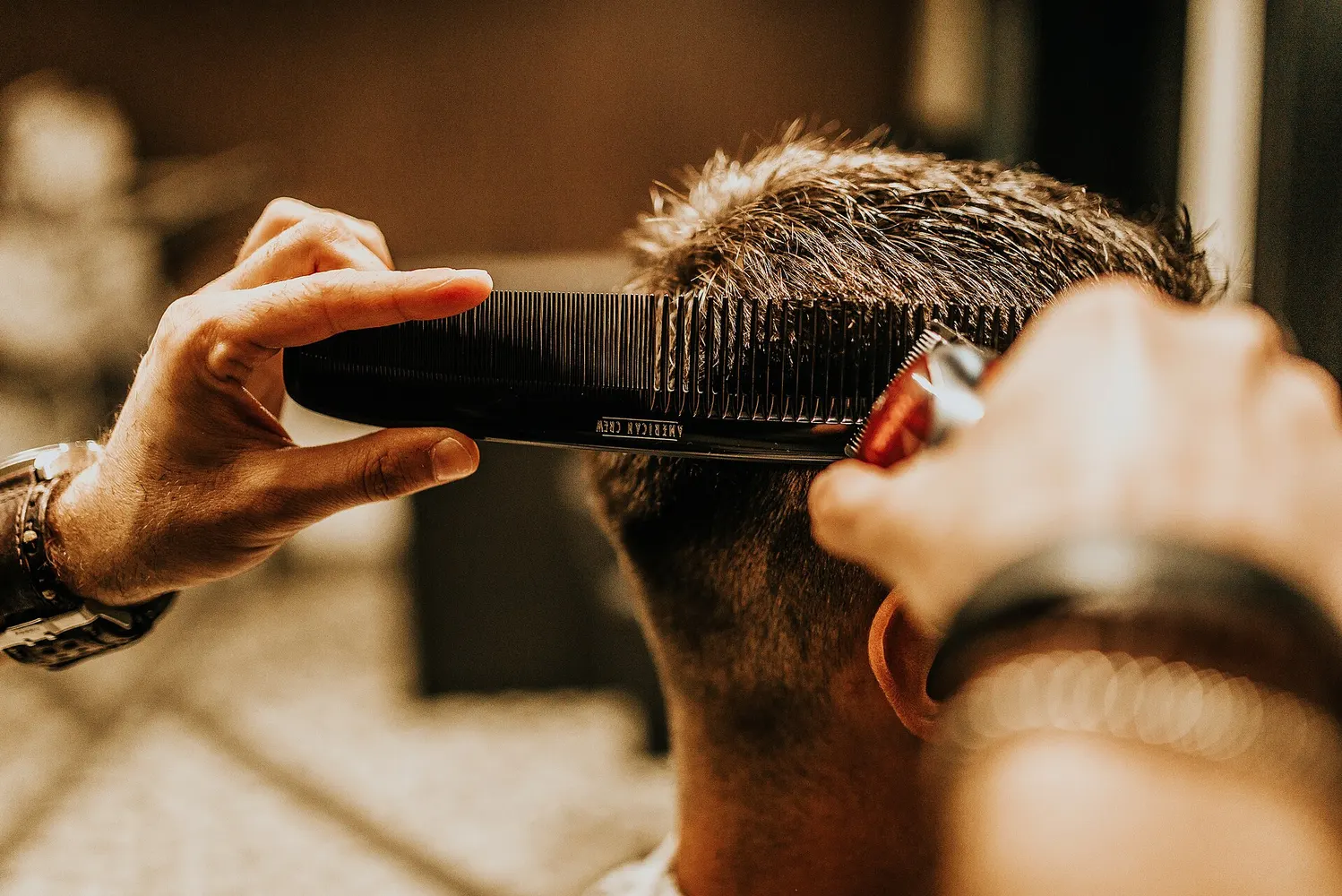 A barber trims a client's hair with a comb and clippers.