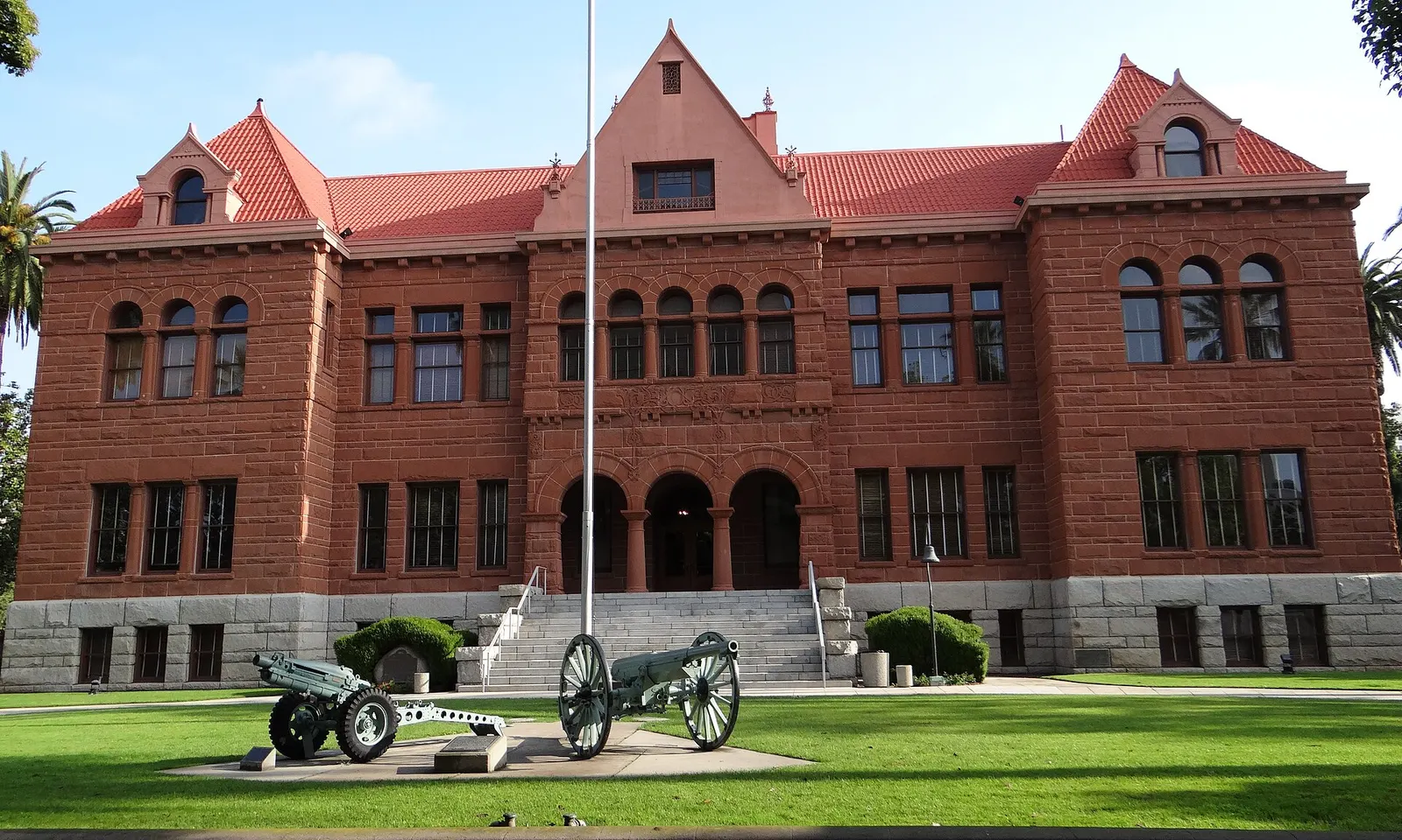 The red sandstone Old Orange County Courthouse in Santa Ana with a lawn and flagpole in front.